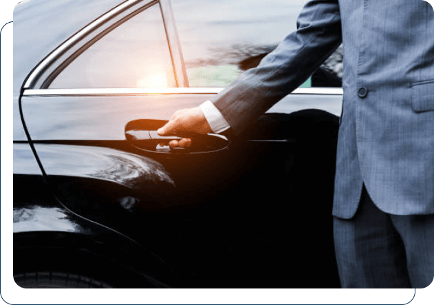 A person in a suit opening the door of a luxury black car.