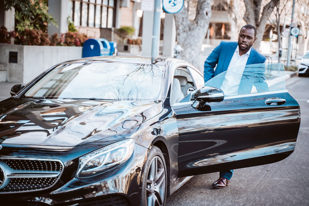 Man in a blue suit getting out of a sleek black luxury sedan, embodying sophistication for a special occasion.